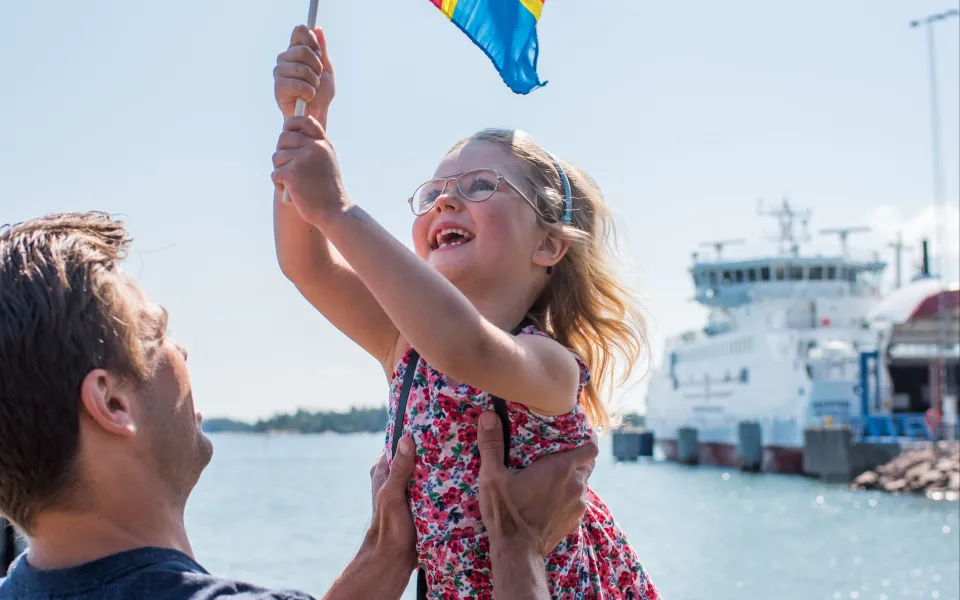 Pappa barn med ålandsflagga, skärgårdsfärja i bakgrunden